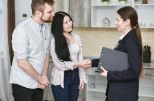 A young couple shakes hands with a real estate agent during a home tour or negotiation in a modern setting.